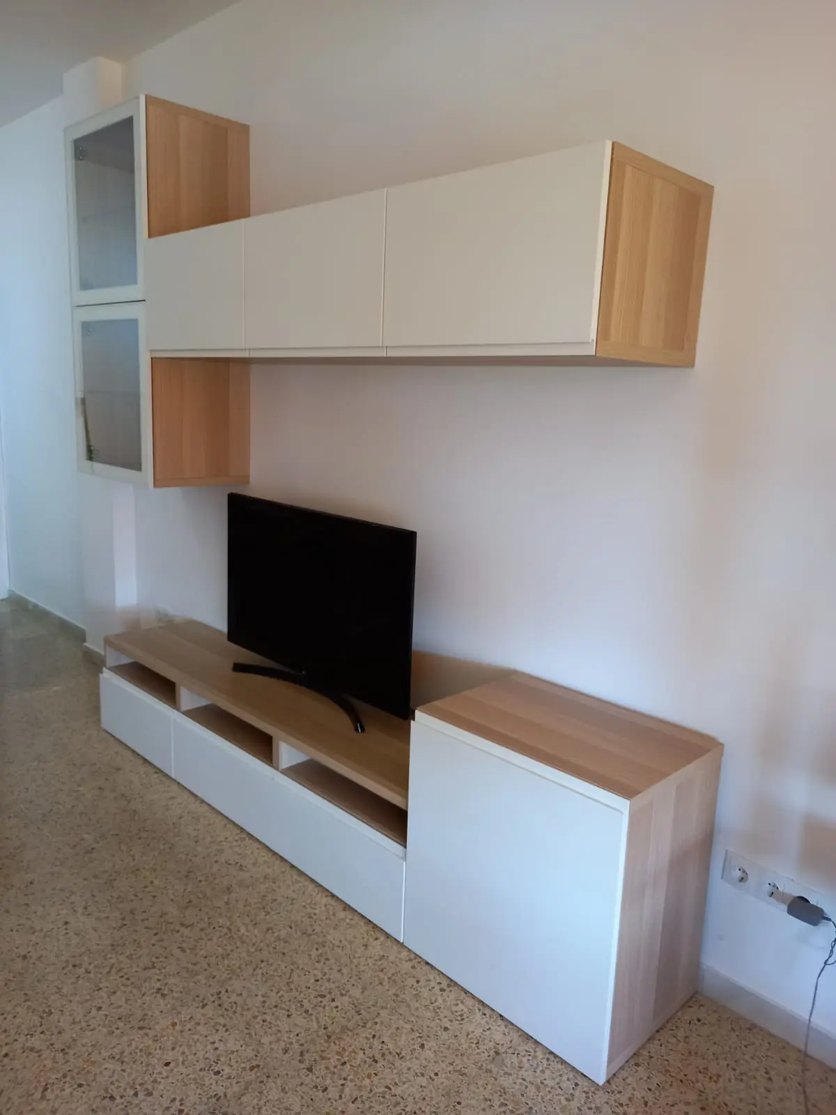 Mueble de salón blanco y madera con módulos colgados en la pared y mueble bajo para la tele